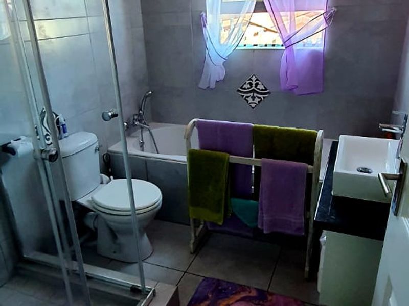 A functional bathroom featuring a glass shower enclosure, a bathtub, a toilet, and a vanity basin with neutral wall and floor tiling.