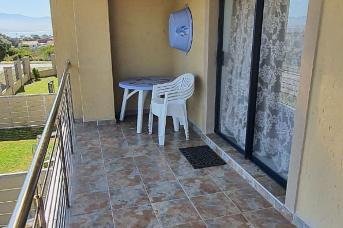 A covered balcony featuring tiled flooring, a stainless steel balustrade, and a timber pergola, offering an outdoor space with sliding door access.