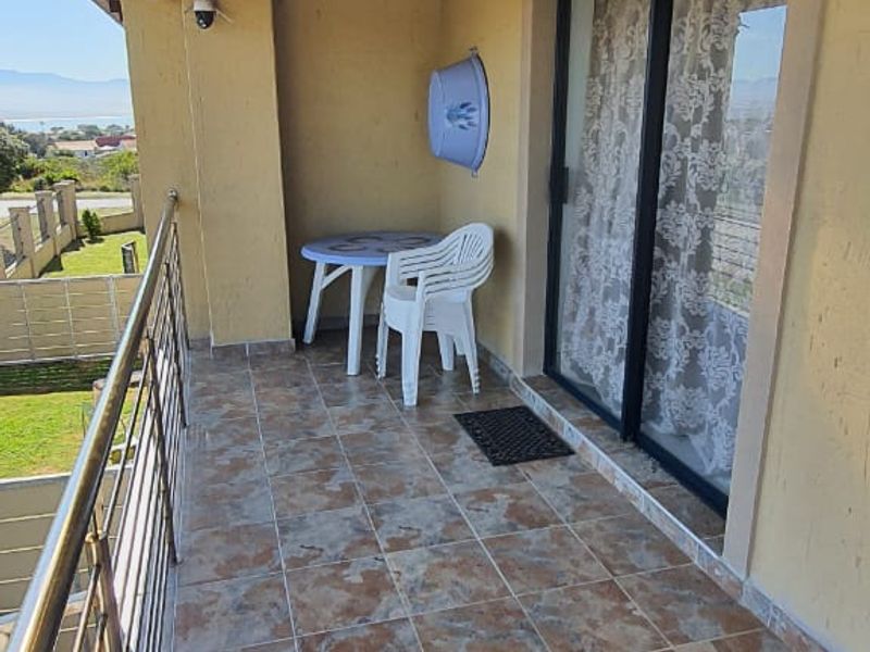 A covered balcony featuring tiled flooring, a stainless steel balustrade, and a timber pergola, offering an outdoor space with sliding door access.