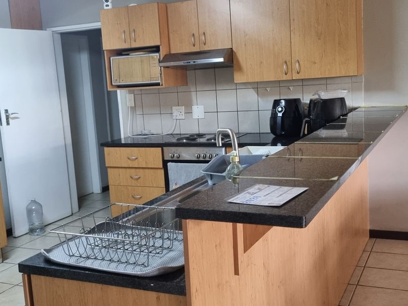 Functional kitchen featuring laminate cabinetry, granite countertops, built-in oven, electric hob, and a breakfast bar counter.