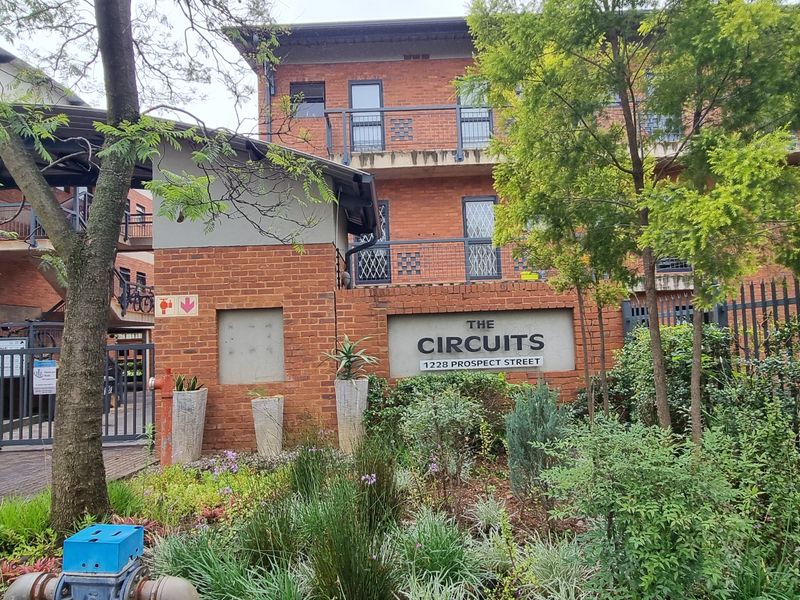 Front elevation of The Circuits apartment complex, featuring a brick facade, secure gated entrance, and landscaped garden area.
