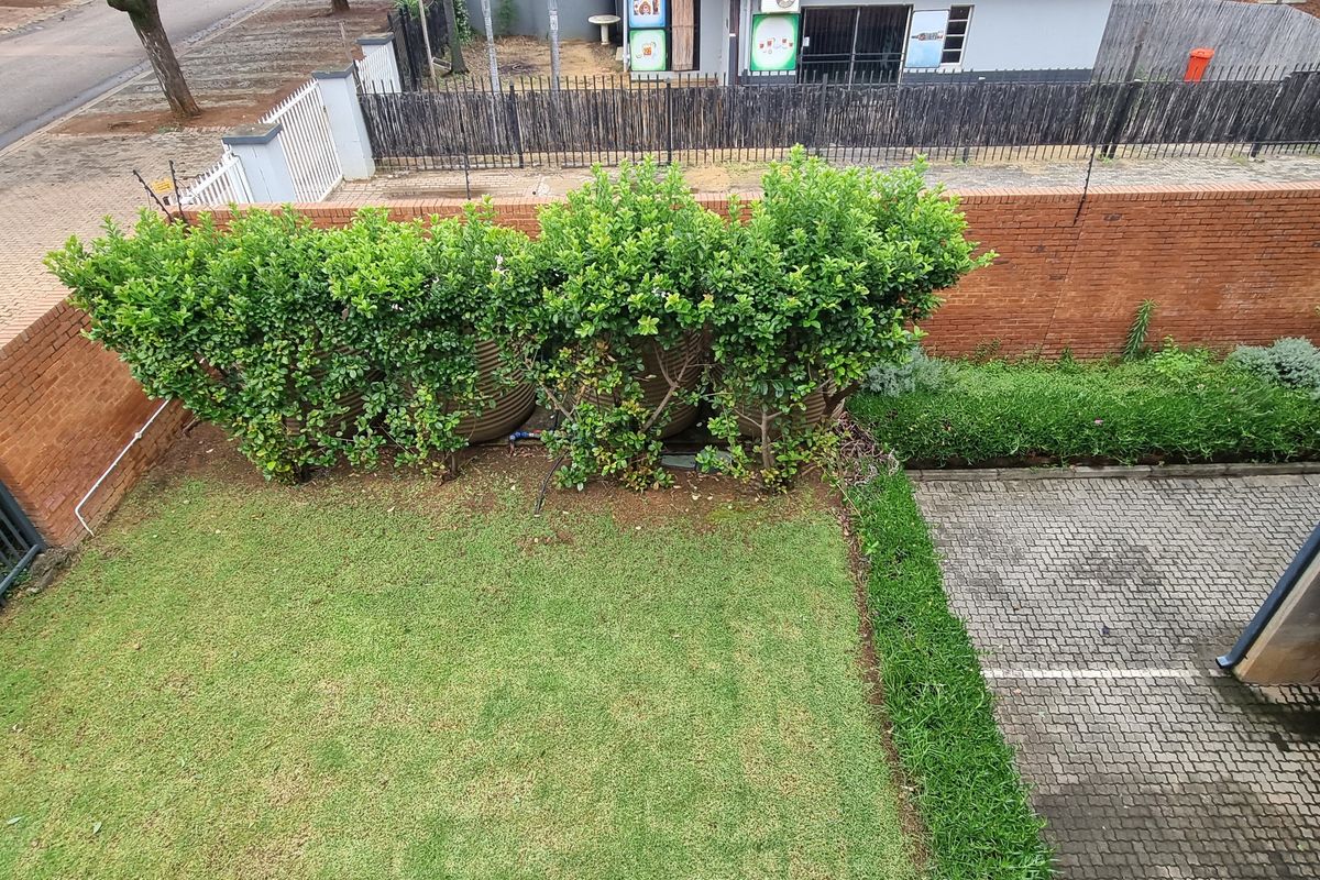 An elevated view of a private rear garden featuring a lawn, paved area, and brick boundary wall with integrated electric fencing.