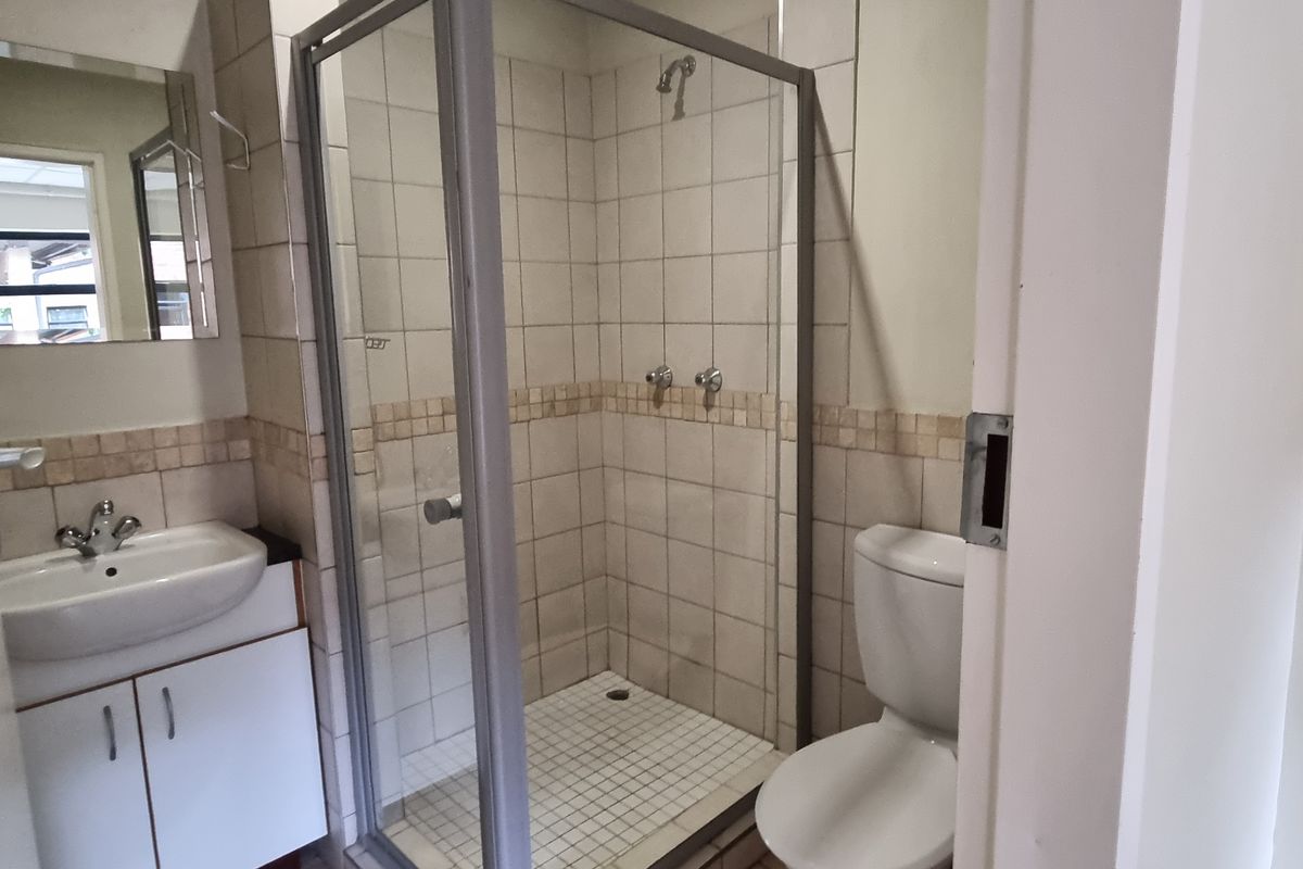 A functional bathroom featuring a shower enclosure, vanity basin with cabinet, and a toilet, finished with neutral wall tiling.