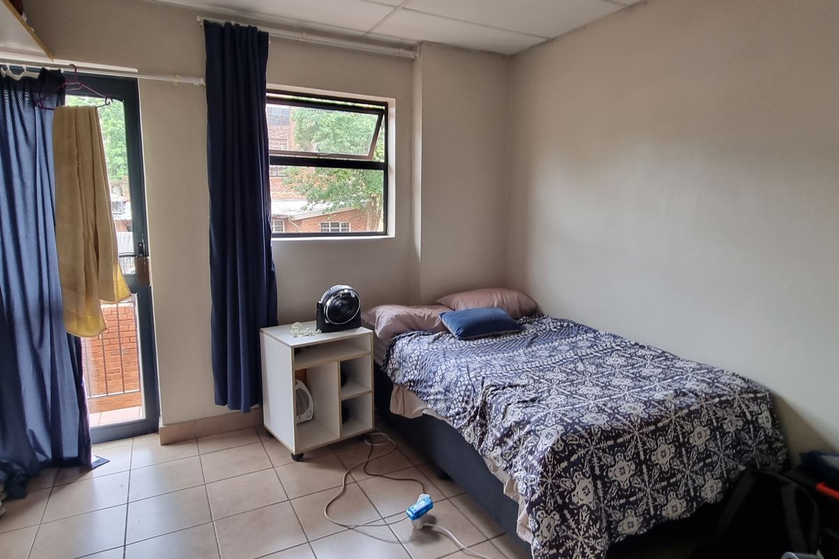 A bedroom featuring tiled flooring, a window, and a sliding door providing access to a small balcony.