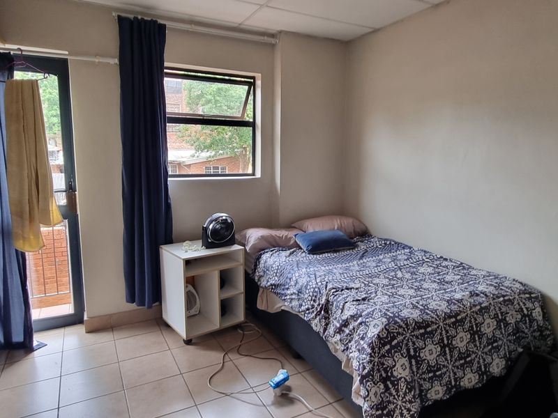 A bedroom featuring tiled flooring, a window, and a sliding door providing access to a small balcony.