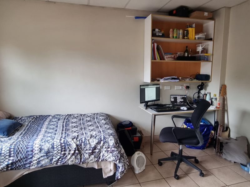 A functional bedroom featuring tiled flooring, a built-in wardrobe, and integrated wall shelving, providing practical storage and living space.