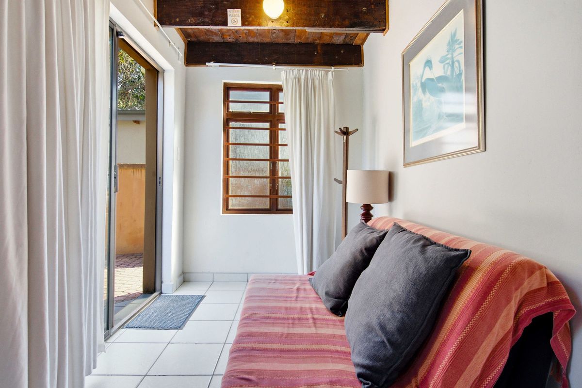 A cozy living area featuring exposed timber ceiling beams, tiled flooring, and a sliding glass door providing direct access to the outdoor patio.
