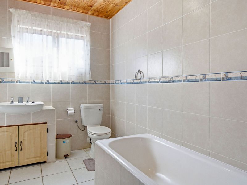 A functional bathroom featuring a built-in vanity, bathtub, toilet, and neutral wall tiling with a timber ceiling finish.