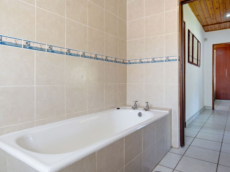 A functional bathroom featuring a built-in bathtub with tiled surround and neutral wall tiling, leading into a hallway with built-in storage.