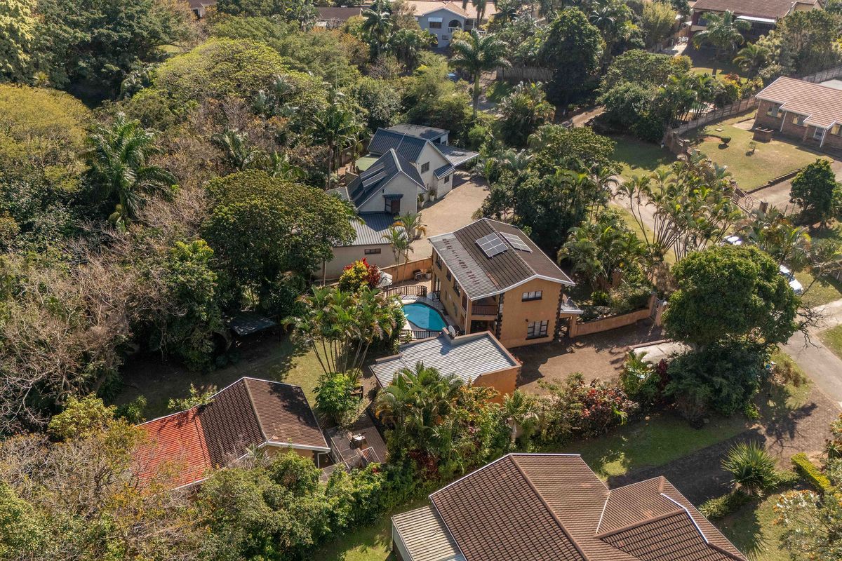 Aerial view of the property showcasing the main residence, swimming pool, surrounding landscaped gardens, and multiple outbuildings within a lush residential setting.
