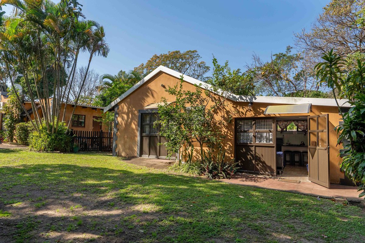 A view of the rear exterior of the house featuring a stucco facade, tiled roof, and a paved patio area leading into the garden.
