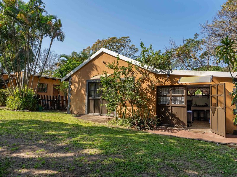A view of the rear exterior of the house featuring a stucco facade, tiled roof, and a paved patio area leading into the garden.
