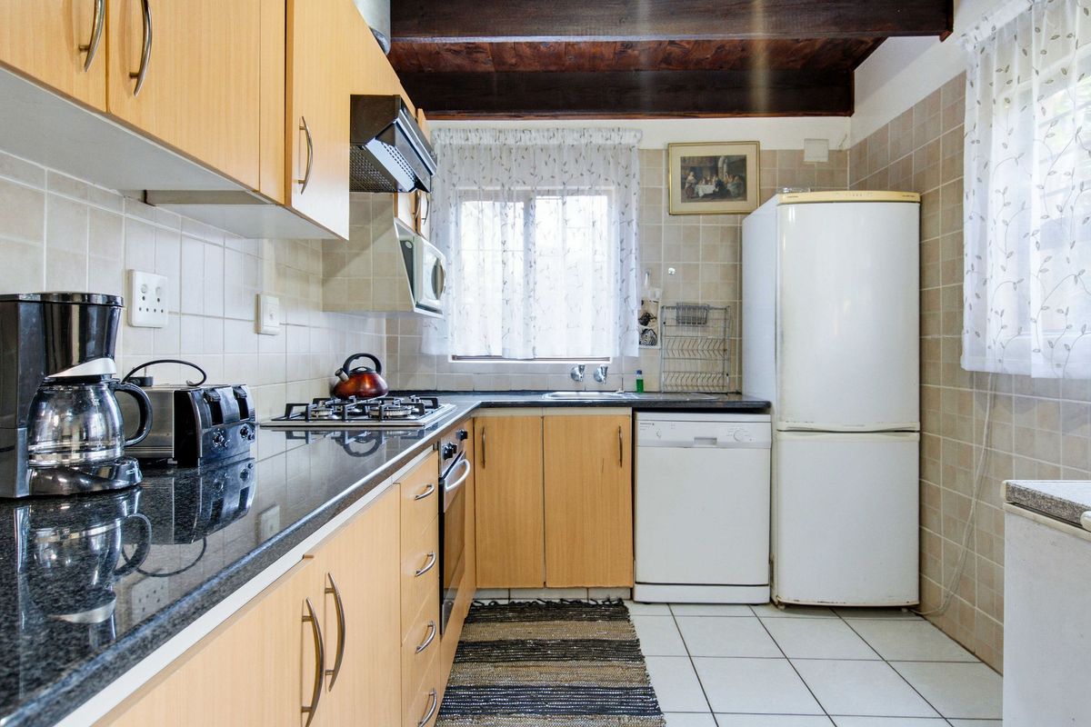 A functional kitchen featuring laminate cabinetry, granite countertops, a gas hob, built-in oven, and exposed timber ceiling beams with tiled finishes.