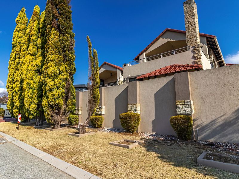 Street view of the property featuring a high boundary wall with stone accents, tiled roof, and an elevated balcony.