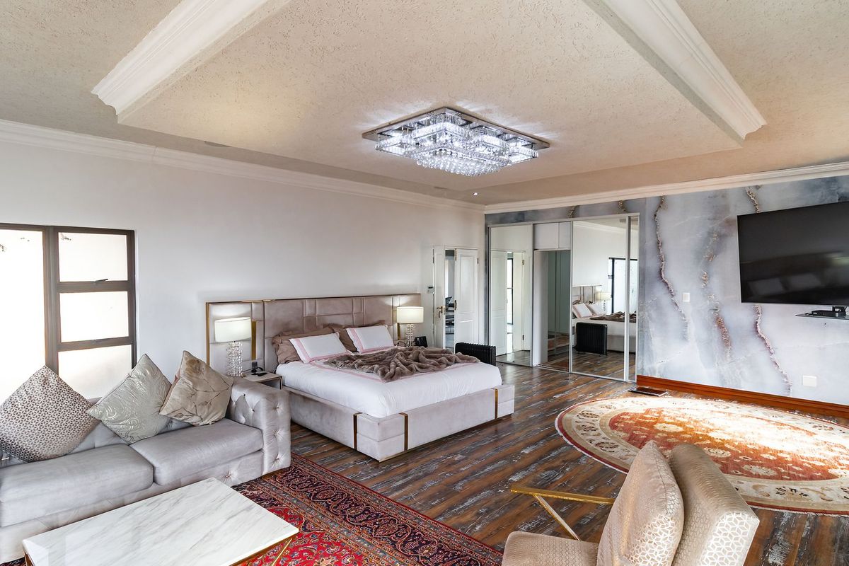 Spacious bedroom featuring a tray ceiling with crystal chandelier, mirrored built-in wardrobes, and a striking marble-effect feature wall.