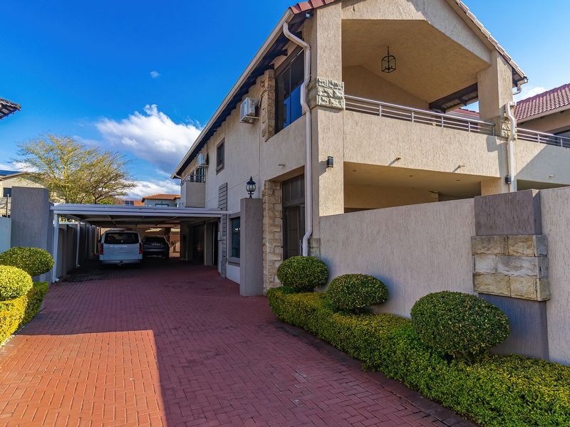 Front elevation of a multi-story residential property featuring a paved driveway, covered carport, and a spacious upper-level balcony with stone cladding accents.