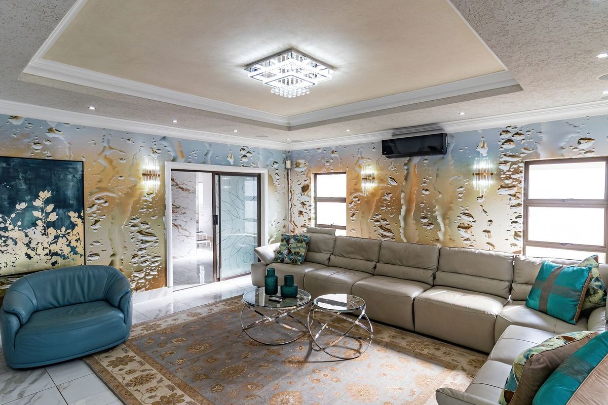 Spacious living room featuring a recessed ceiling with crystal chandelier, split-system air conditioning, and tiled flooring with decorative wall finishes.