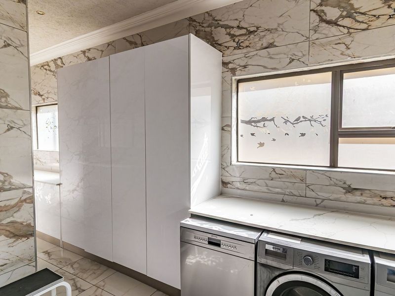 Modern laundry room featuring high-gloss white cabinetry, marble-look wall tiling, stone countertops, and integrated appliances.