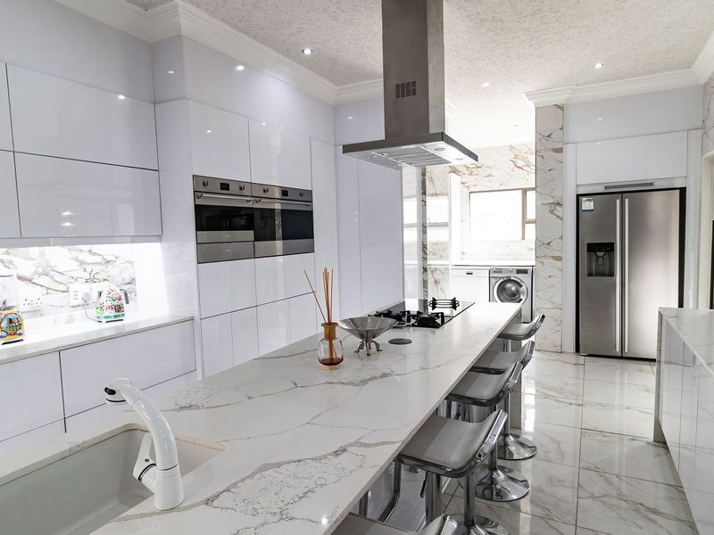 Modern, high-end kitchen featuring sleek white high-gloss cabinetry, marble-look quartz countertops, a central island with breakfast bar, and integrated stainless steel appliances.