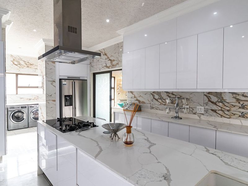 Modern kitchen featuring high-gloss white cabinetry, marble-look quartz countertops, a central island with a gas hob, and integrated appliances.