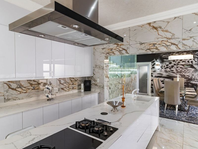 Modern open-plan kitchen featuring high-gloss cabinetry, marble-look porcelain surfaces, a central island with gas cooktop, and integrated high-end finishes.