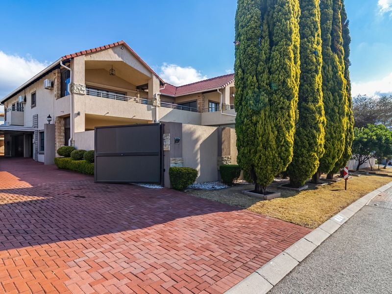 A well-maintained double-story residence featuring a brick-paved driveway, secure automated gate access, and multiple balconies with a tiled roof.