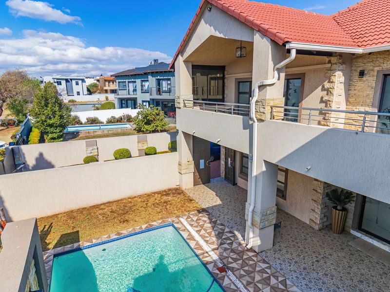 Rear view of a double-story house featuring a swimming pool, covered patio, upper balcony, and stone-clad architectural details.