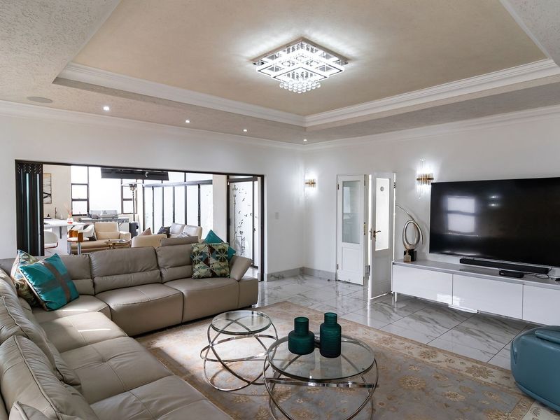 Spacious living room featuring a tray ceiling with recessed lighting, a crystal chandelier, and polished marble tile flooring, opening to an adjacent patio area.
