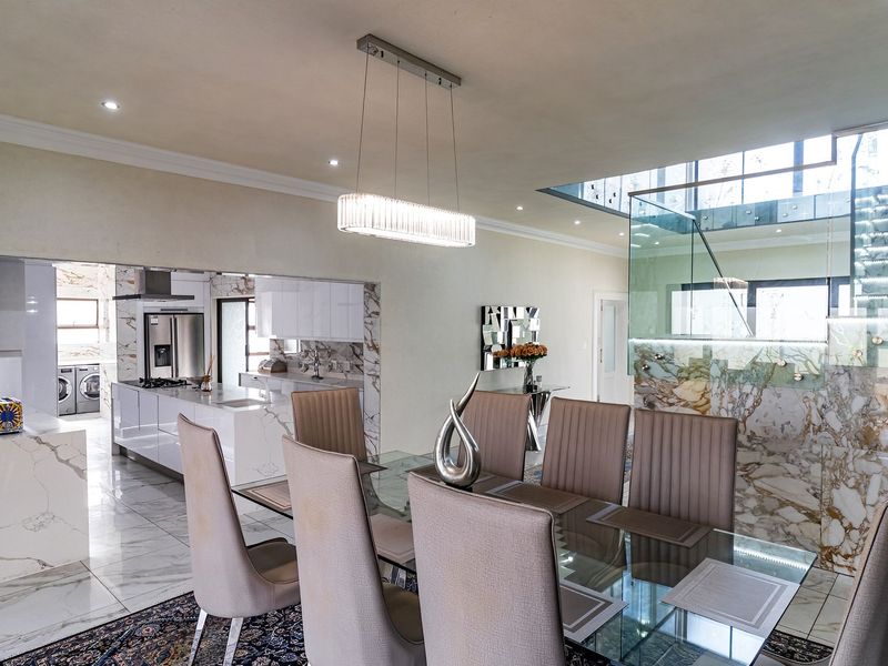 Spacious open-plan dining and kitchen area featuring luxurious marble flooring, striking marble wall accents, and a modern glass staircase with integrated lighting.