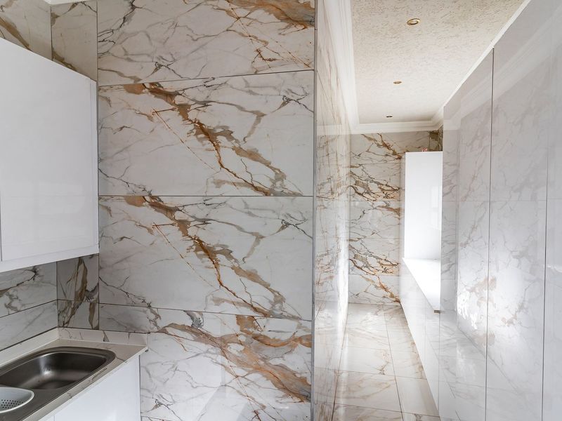 A modern, high-end scullery or utility area featuring premium marble-look wall and floor tiling, sleek built-in cabinetry, and a brass faucet fixture.