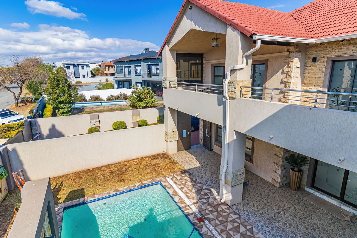 Rear view of a double-story house featuring a swimming pool, covered patio, upper balcony, and stone-clad architectural details.