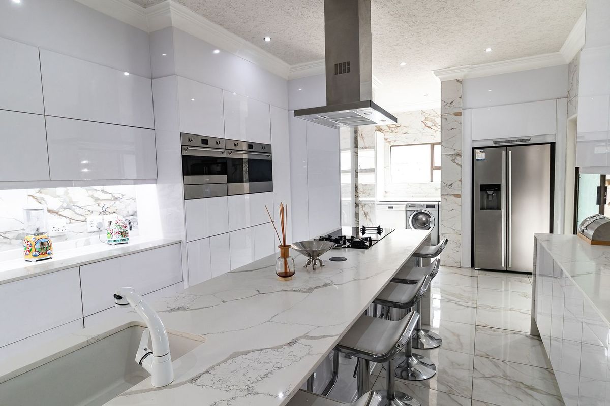 Modern, high-end kitchen featuring sleek white high-gloss cabinetry, marble-look quartz countertops, a central island with breakfast bar, and integrated stainless steel appliances.