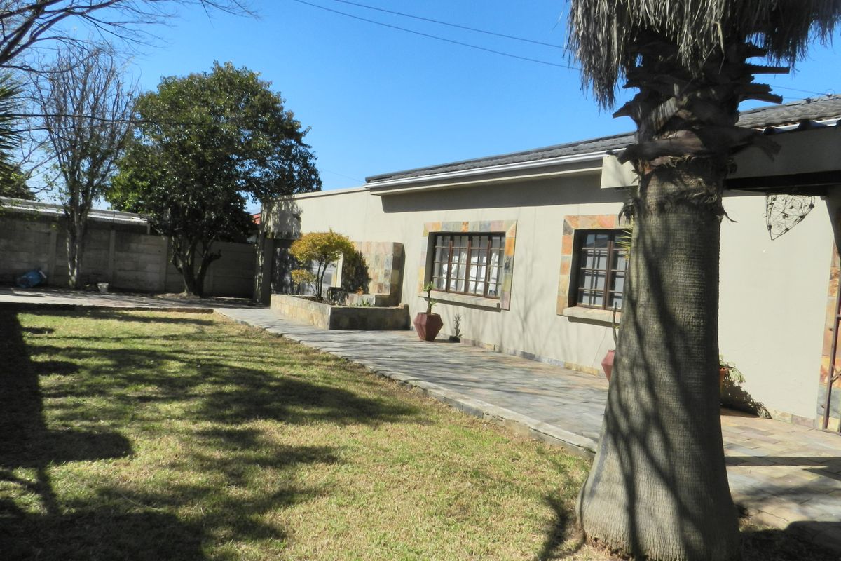Rear view of the house featuring a paved patio area, stone-clad accents, and a spacious garden with established trees and boundary walling.