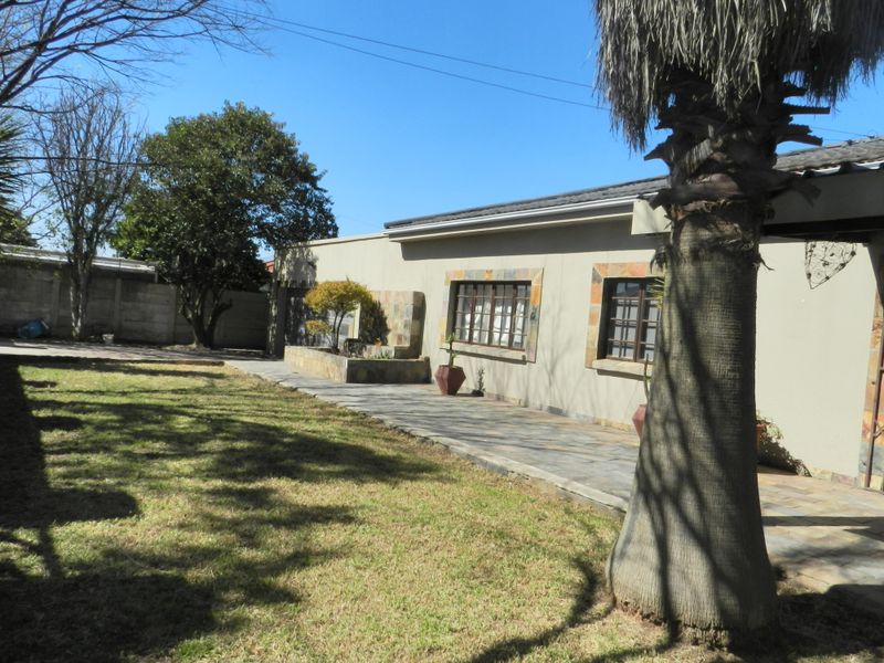 Rear view of the house featuring a paved patio area, stone-clad accents, and a spacious garden with established trees and boundary walling.