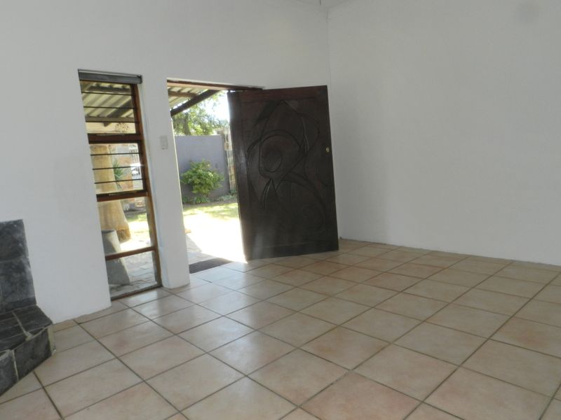 An empty living room featuring tiled flooring, a built-in fireplace, and a wooden entrance door leading to the exterior.