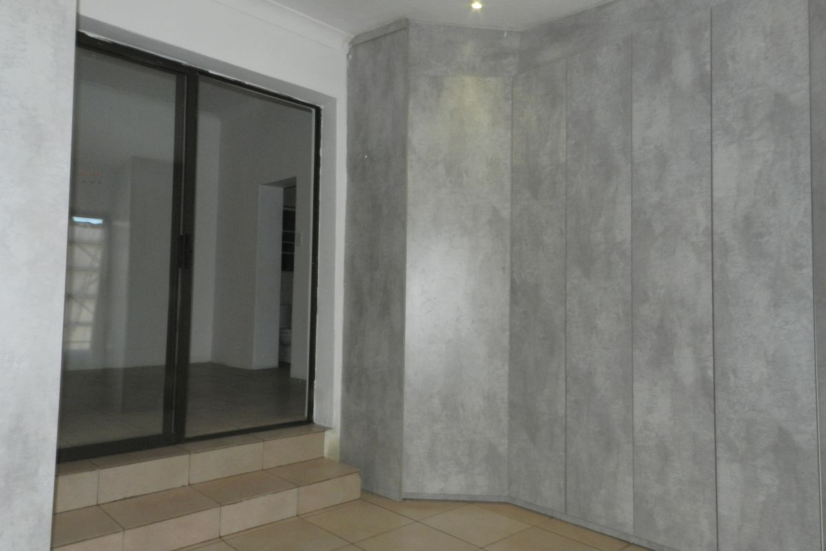 A clean, empty bedroom featuring modern grey built-in cupboards, tiled flooring, and a sliding glass door leading to an adjacent space.