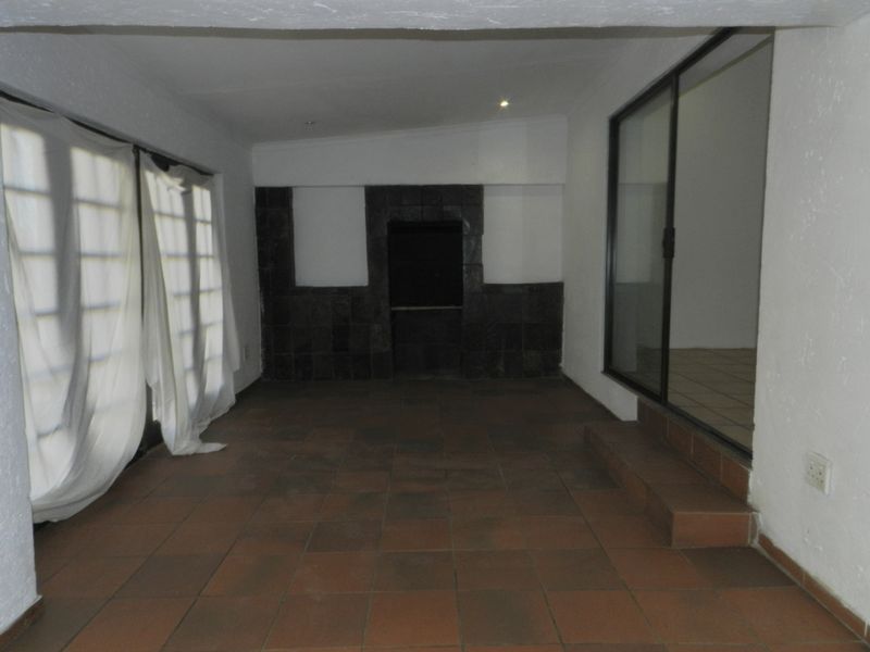 An empty covered patio area featuring tiled flooring, a built-in braai, and sliding glass doors providing access to the interior living space.