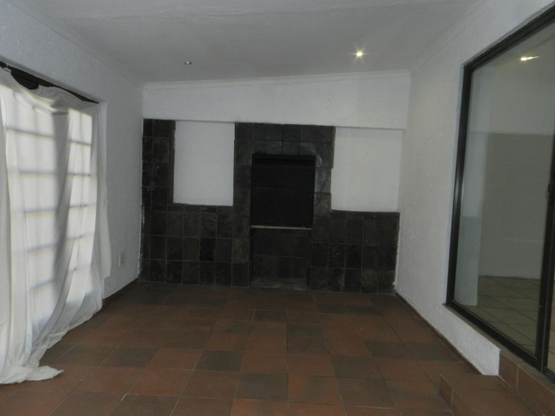 An empty covered patio area featuring a built-in braai, tiled flooring, and large sliding glass doors providing access to the outdoor space.