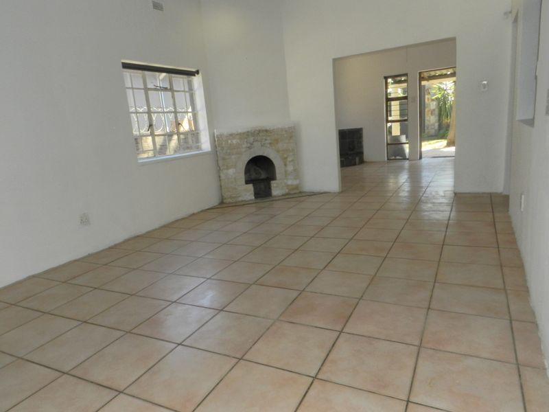 An empty living room featuring tiled flooring and a stone fireplace, with an open transition to an adjacent space and outdoor access.