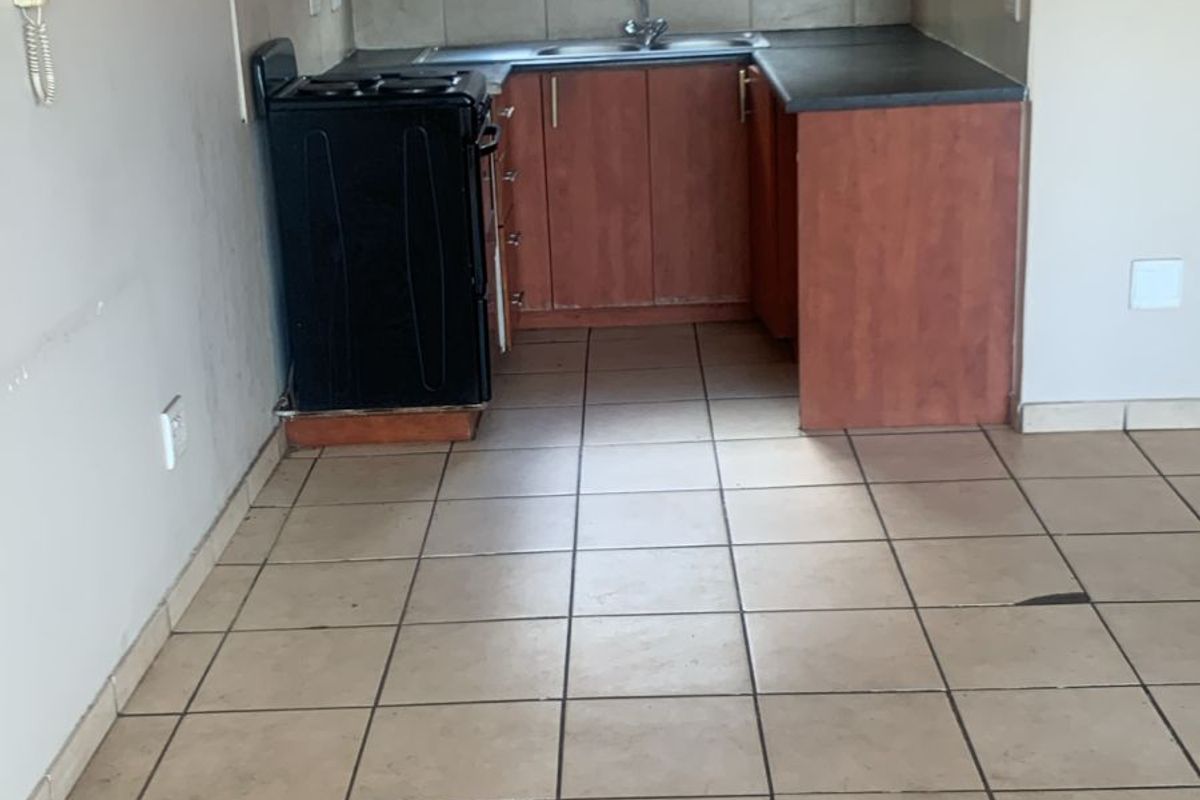 A compact, empty kitchen featuring wooden cabinetry, laminate countertops, a stainless steel sink, and tiled flooring, offering a functional space ready for updates.