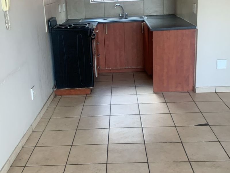 A compact, empty kitchen featuring wooden cabinetry, laminate countertops, a stainless steel sink, and tiled flooring, offering a functional space ready for updates.