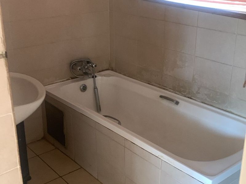 A dated bathroom featuring a standard bathtub, pedestal basin, and tiled finishes, requiring cosmetic updates to modernize the space.