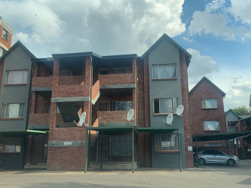 Front elevation of a multi-story face brick apartment complex featuring covered parking bays, external staircases, and private balconies.