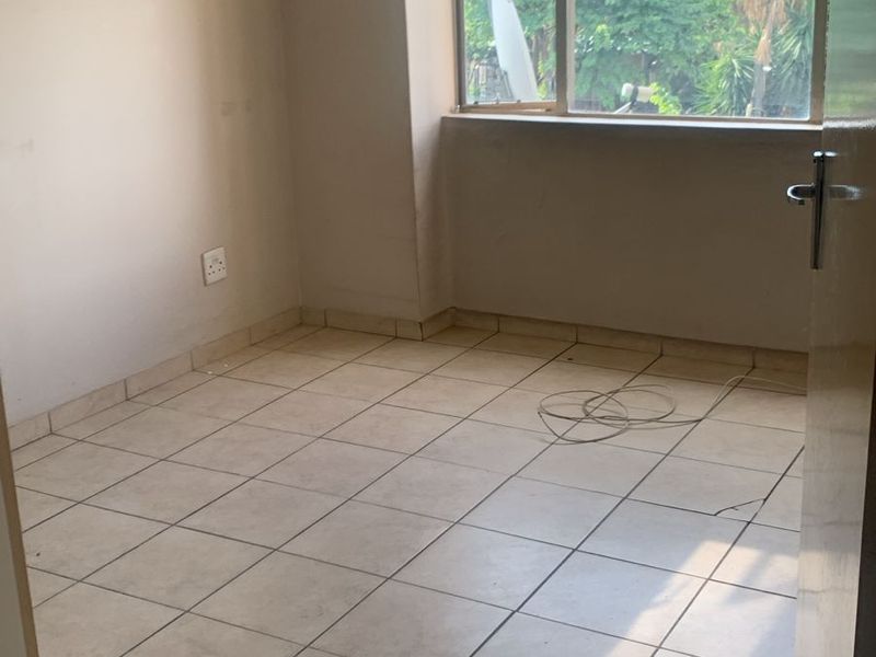 An empty bedroom featuring tiled flooring and a window with natural light, ready for renovation or staging.