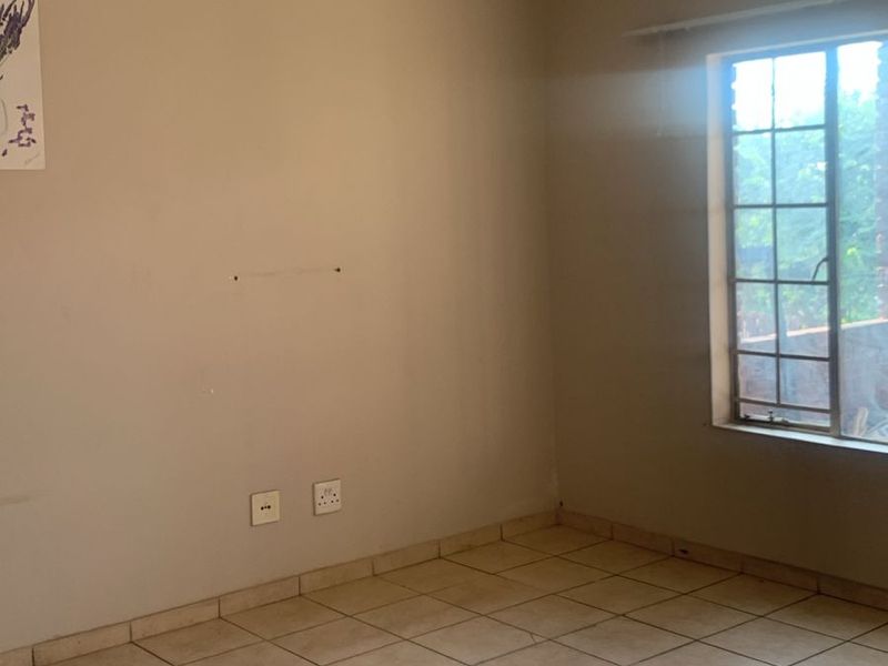 An empty bedroom featuring neutral wall paint, ceramic floor tiles, and a steel-framed window, providing a blank canvas for interior design.