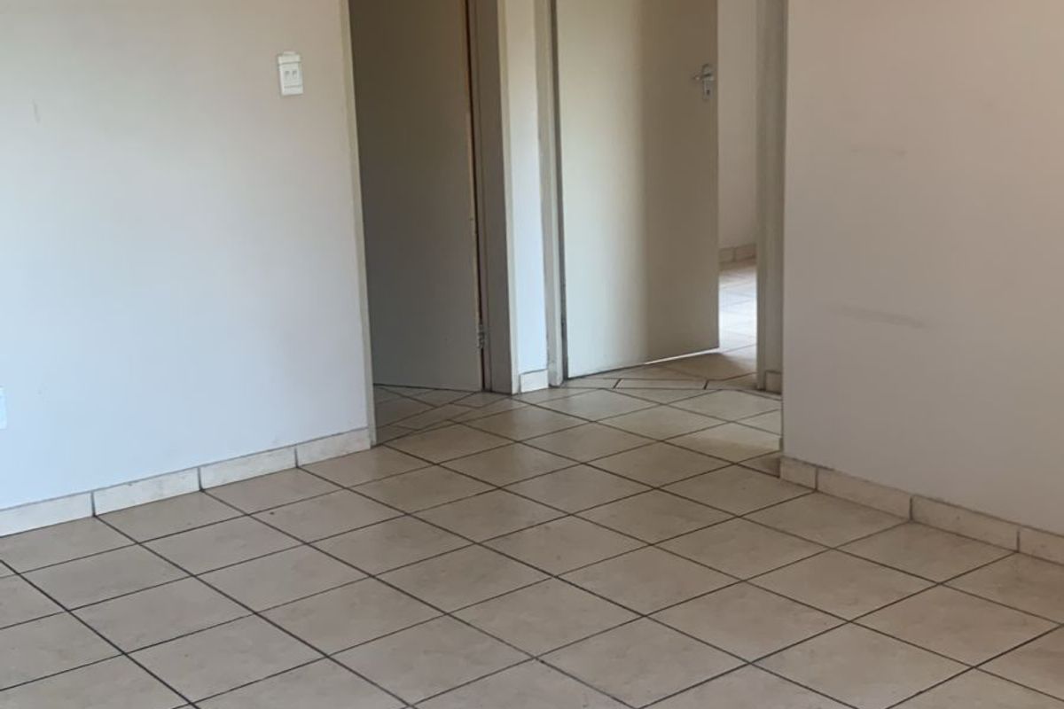 An empty living area featuring neutral wall paint and ceramic floor tiles, providing a blank canvas for interior design.
