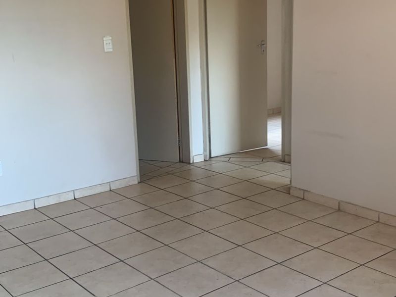An empty living area featuring neutral wall paint and ceramic floor tiles, providing a blank canvas for interior design.