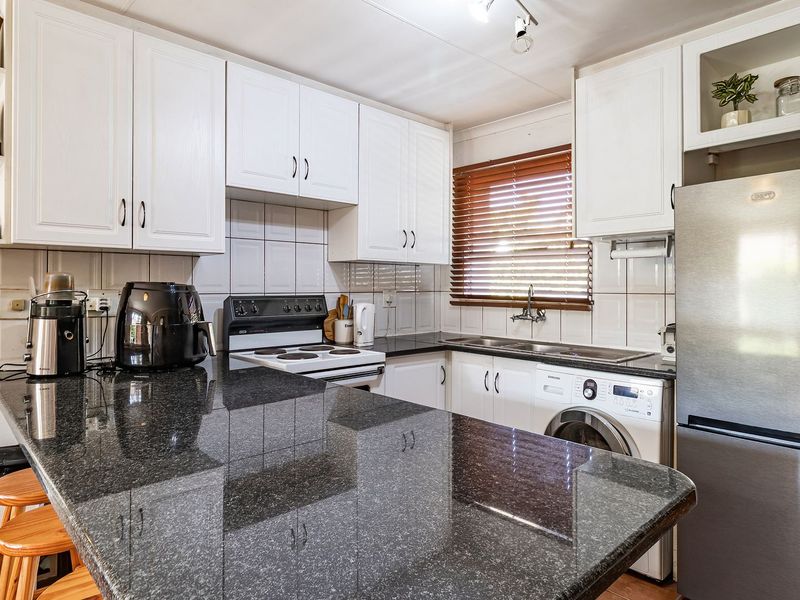 A functional kitchen featuring granite countertops, white cabinetry, tiled backsplash, and integrated appliances including a washing machine and oven.