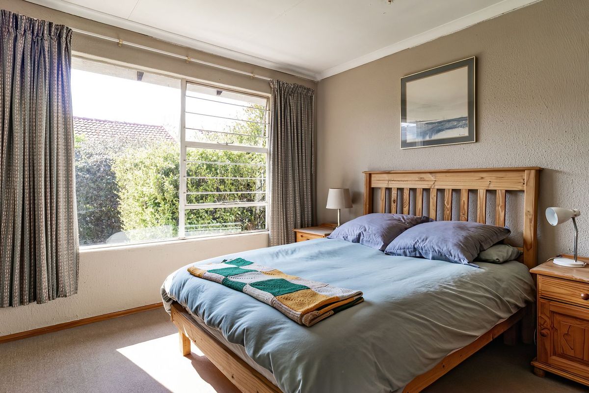A well-lit bedroom featuring a large window with natural light, neutral wall finishes, and carpeted flooring.