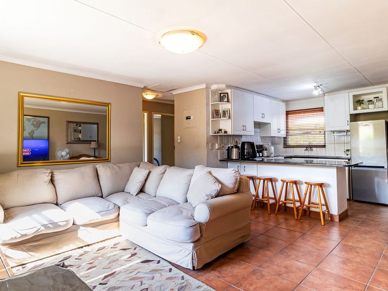 Open-plan living and kitchen area featuring tiled flooring, white cabinetry, and a breakfast bar, creating a functional and connected living space.